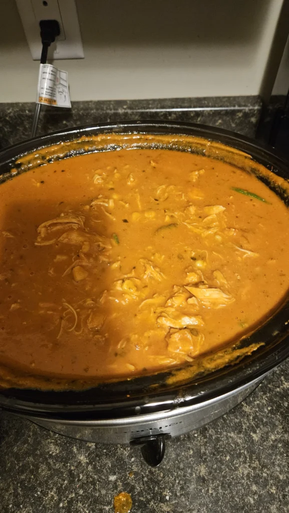 A crock pot full to the brim with butter chicken.