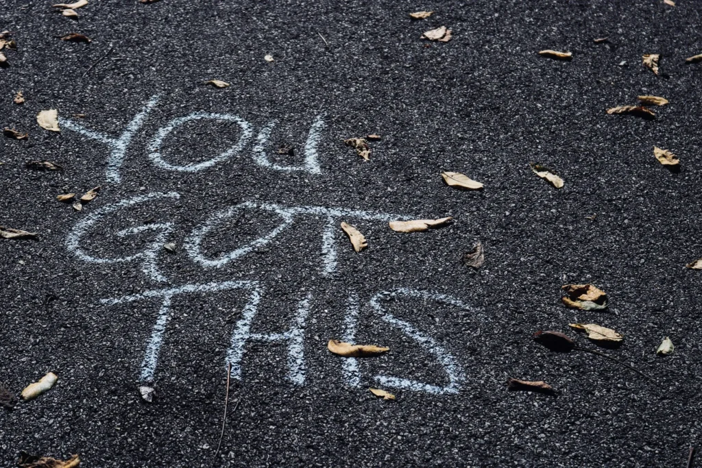 A stock image of chalk on a road that says YOU GOT THIS with some dried leaves scattered around